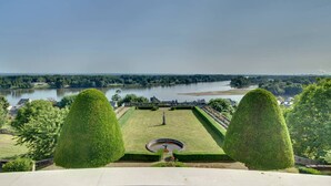 Un jardín ajardinado con un estanque, setos cuidados y vistas a un río y edificios lejanos.