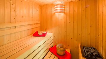 Un sauna en bois avec des bancs, une serviette rouge et un seau rempli de pierres.