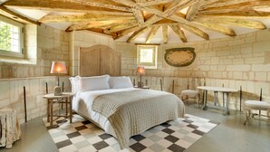 Un dormitorio con piso a cuadros, cama con ropa de cama blanca, dos lámparas de noche, armario de madera y pared de piedra.