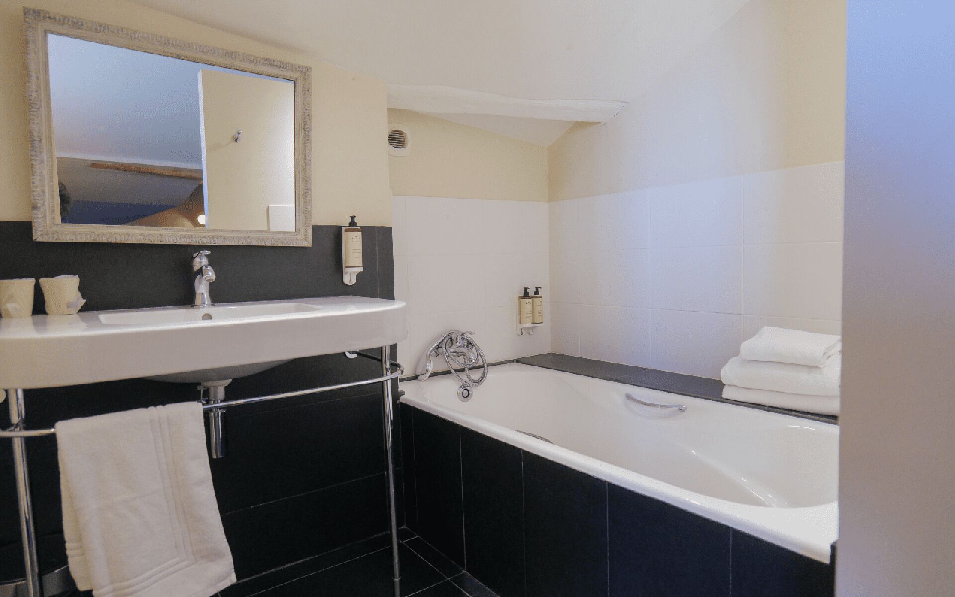 A modern bathroom with a white sink, a large mirror, a bathtub, and black tiles.