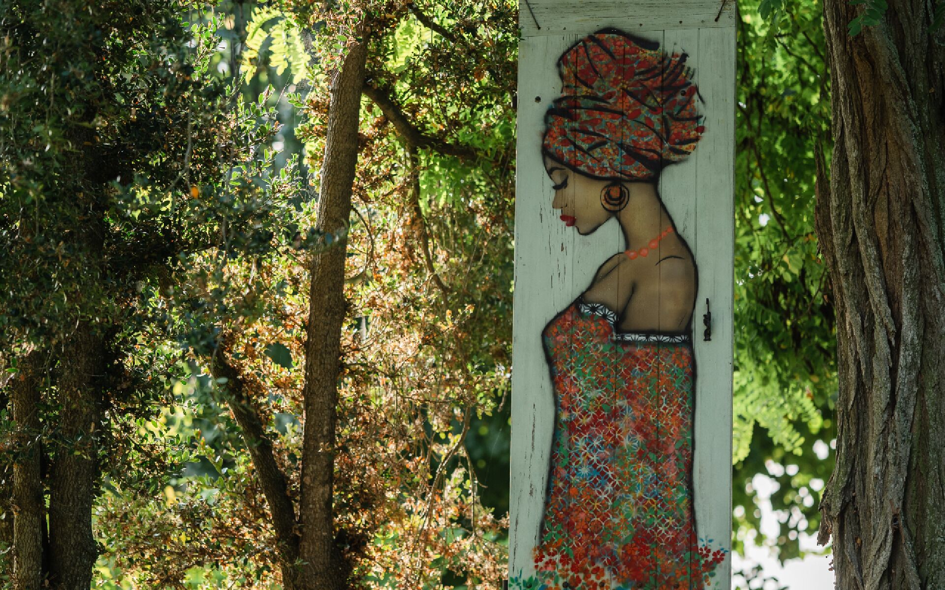 Un mural de una mujer sobre el tronco de un árbol en un bosque.