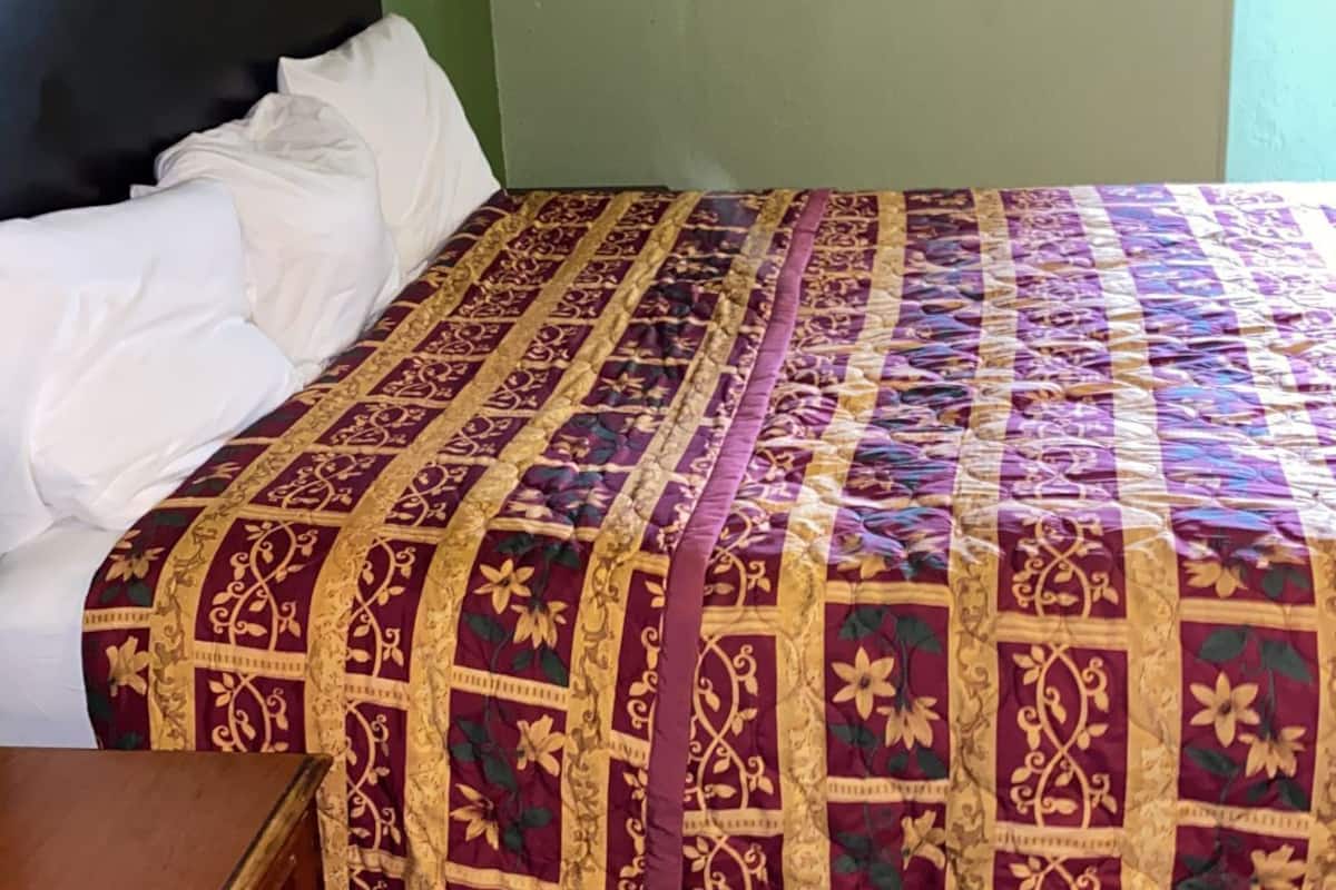 A room with a bed covered by a patterned bedspread, a wooden dresser, and a green wall.