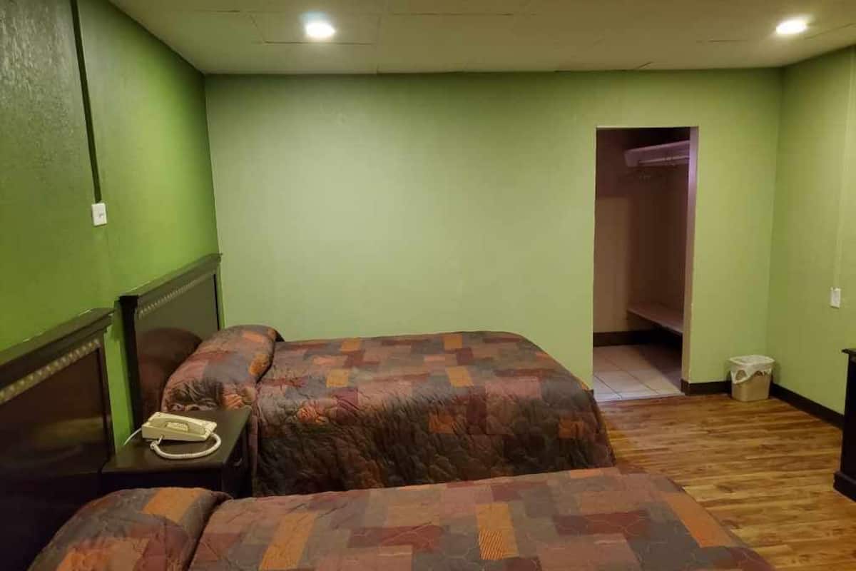 A room with two beds, a wooden floor, a green wall, and a closet.