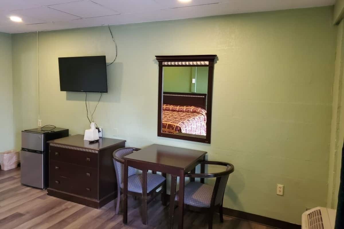 A room with a desk, chair, television, and a mirror.
