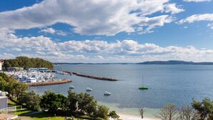 Un port de plaisance avec des bateaux amarrés, une jetée et une vue sur l’eau et les collines lointaines.