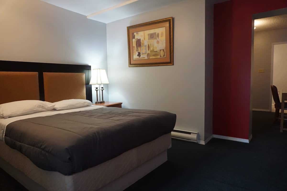 Une chambre d’hôtel avec un lit, une table de chevet avec une lampe, un tableau au mur et un mur d’accent de couleur rouge.