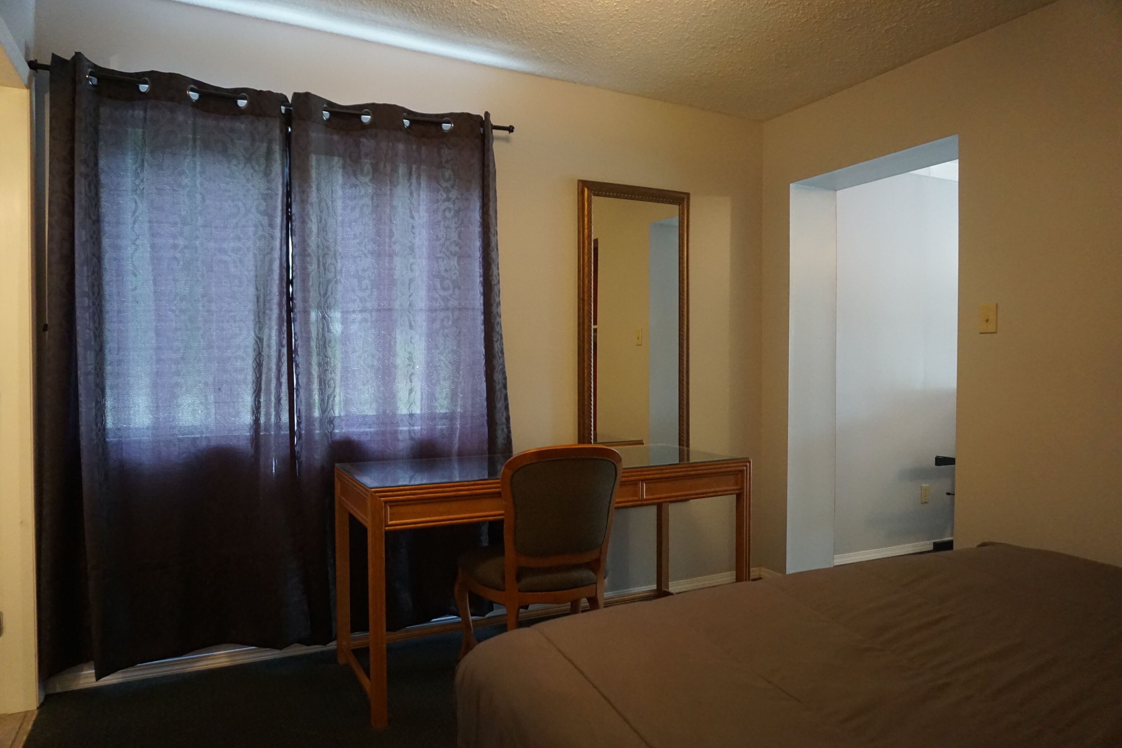 Habitación de hotel con cama, escritorio, silla, espejo y ventana con cortinas.