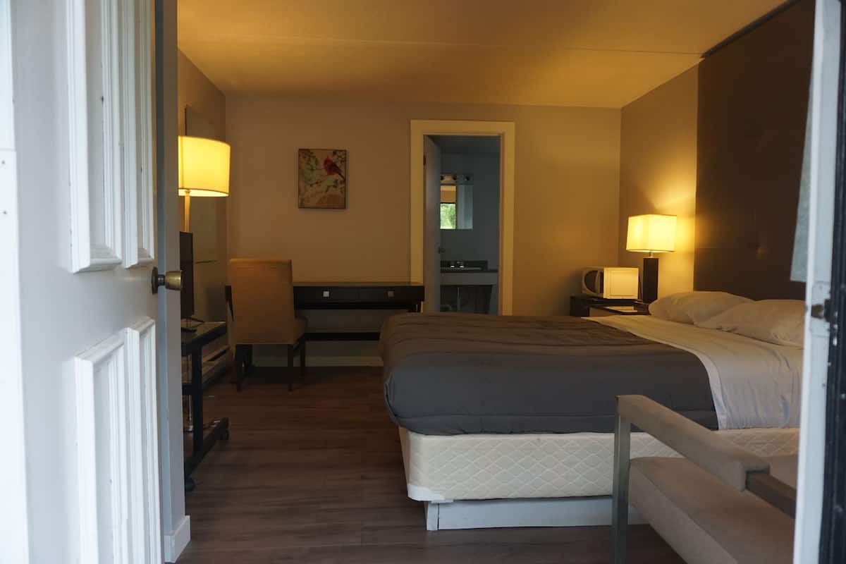 Une chambre d’hôtel comprenant un lit, une table de chevet, une lampe, une chaise et un petit bureau avec une autre chaise.