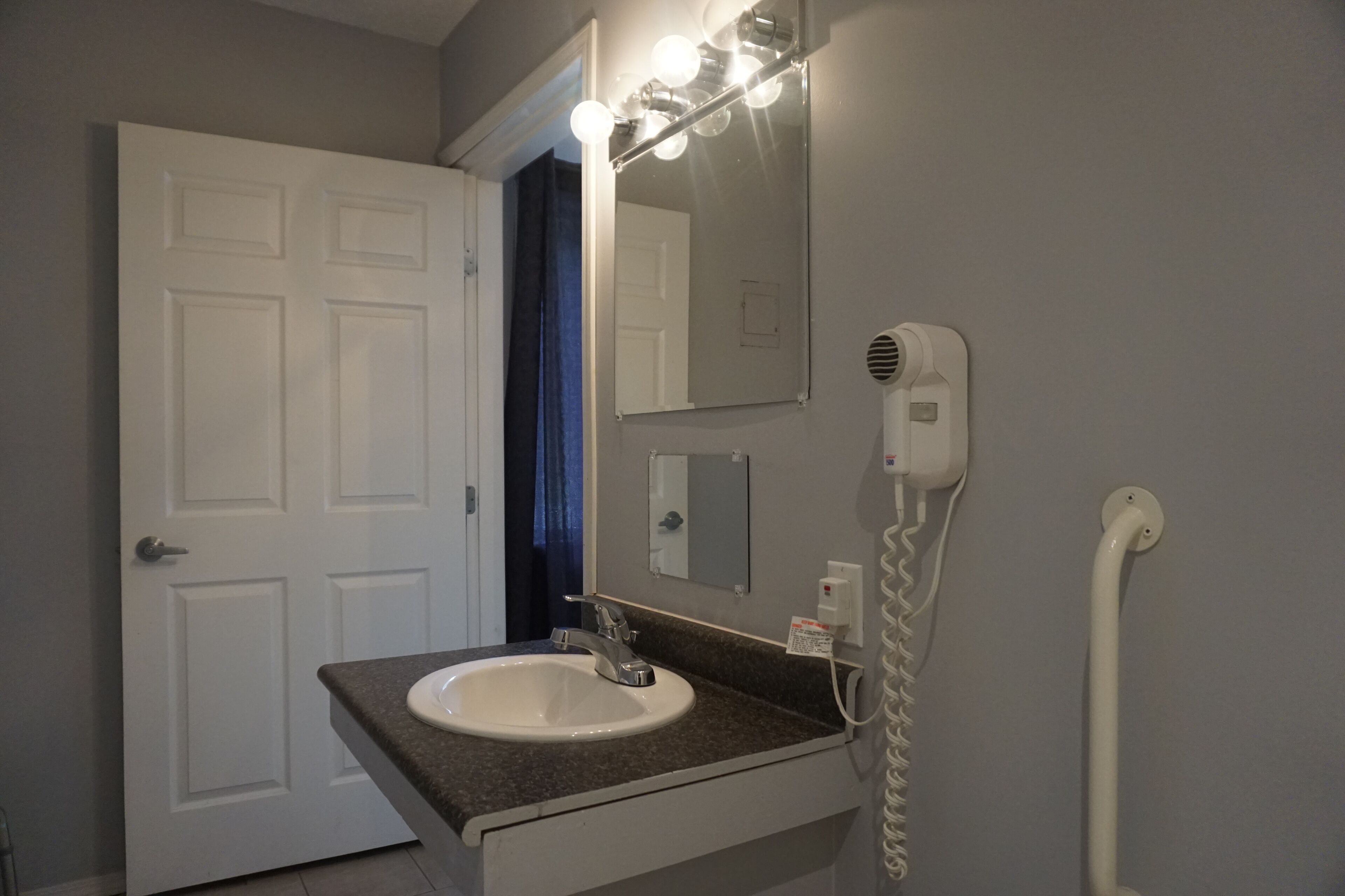 Un baño con un lavamanos blanco, un espejo con iluminación y un secador de pelo.
