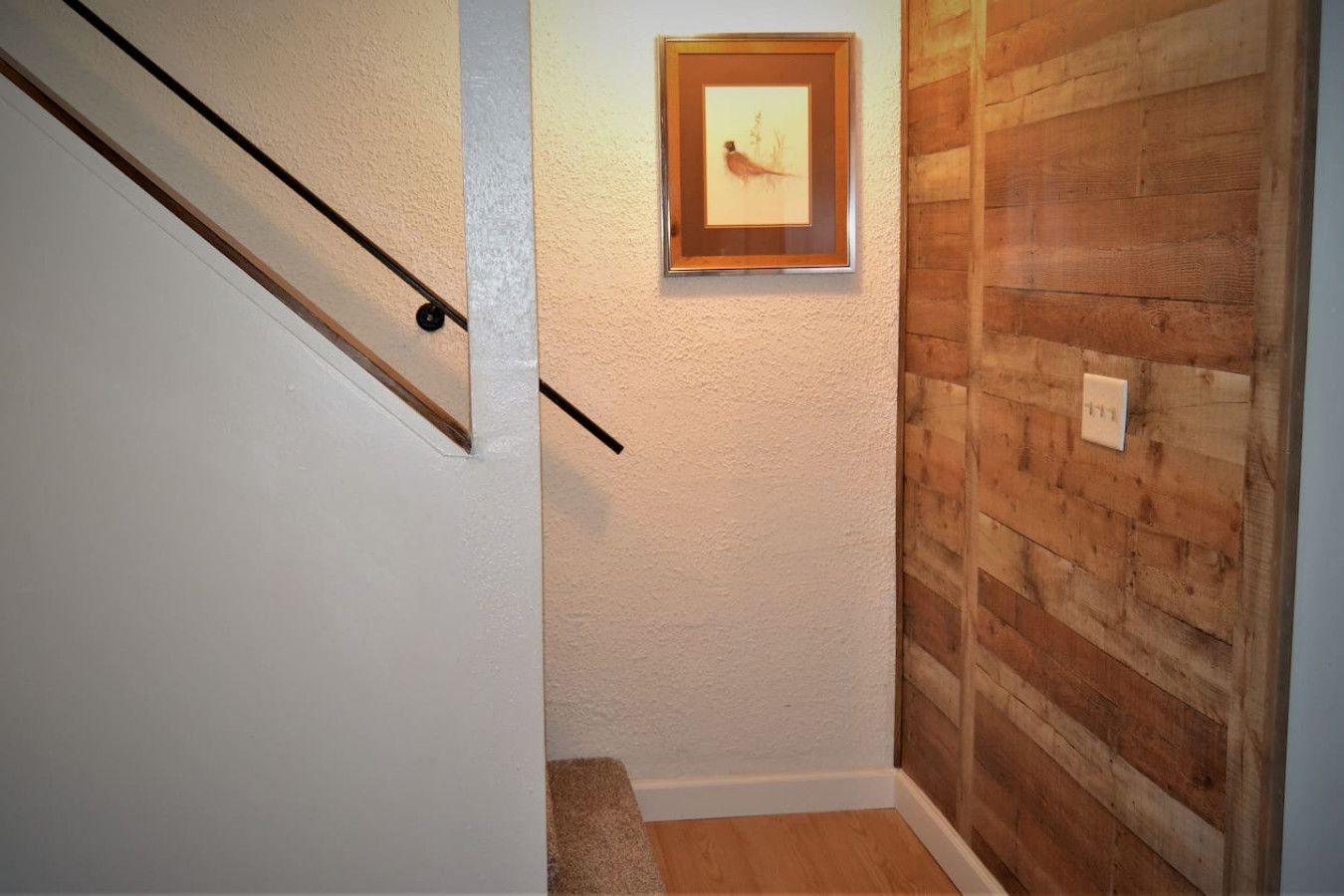 A hallway with a wooden wall, a framed picture, and a staircase.