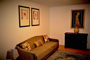 A living room with a sofa, a small cabinet, and framed pictures on the wall. - Urbana – Charming, Bright 2-Bedroom, 1.5-Bath Apartment in the Heart of Grand Forks (Grand Forks)