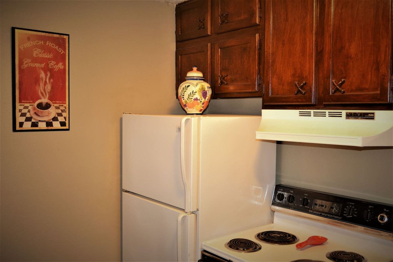 A kitchen with a white refrigerator, a stove with two burners, and wooden cabinets above.