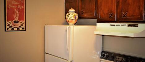 A kitchen with a white refrigerator, a stove with two burners, and wooden cabinets above.