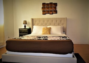 Une chambre à coucher avec un grand lit, une table de chevet, une lampe et une œuvre d’art décorative accrochée au mur au-dessus du lit.