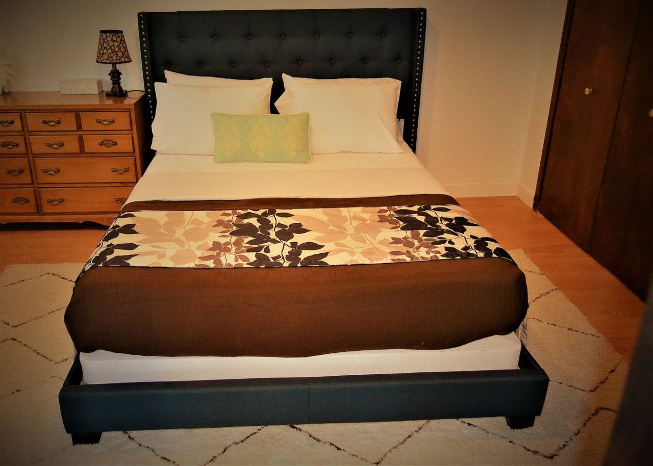 A bed with a dark headboard, white pillows, and a patterned bedspread.