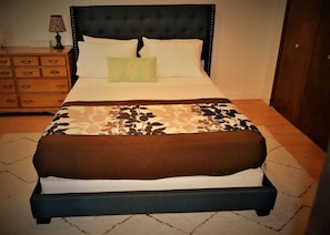 Un lit avec une tête de lit sombre, des oreillers blancs et une couvre-lit à motifs.