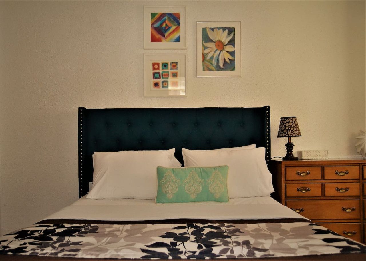 A neatly made bed with a patterned bedspread, a dark upholstered headboard, and a single decorative pillow.