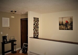 Un couloir avec une machine à café posée sur une table, une porte, une œuvre d’art accrochée au mur et un radiateur.