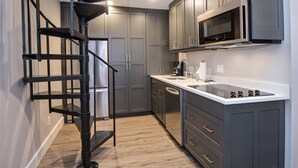 A modern kitchen with grey cabinets, a stainless steel microwave, a built-in oven, and a black spiral staircase. - Unit 14 WITH AC-NEW LOWER PRICE. HEART OF VAIL. WALK TO GONDOLA (Vail)