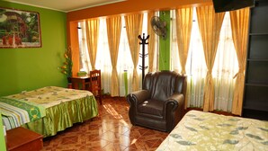 A room with two beds, a chair, a fan, and a window with curtains. - Hospedaje Orbis (Pichanaqui)