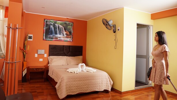 A hotel room with a bed, a wall-mounted fan, a picture of a waterfall, and a door leading to another room. - Hospedaje Orbis (Pichanaqui)
