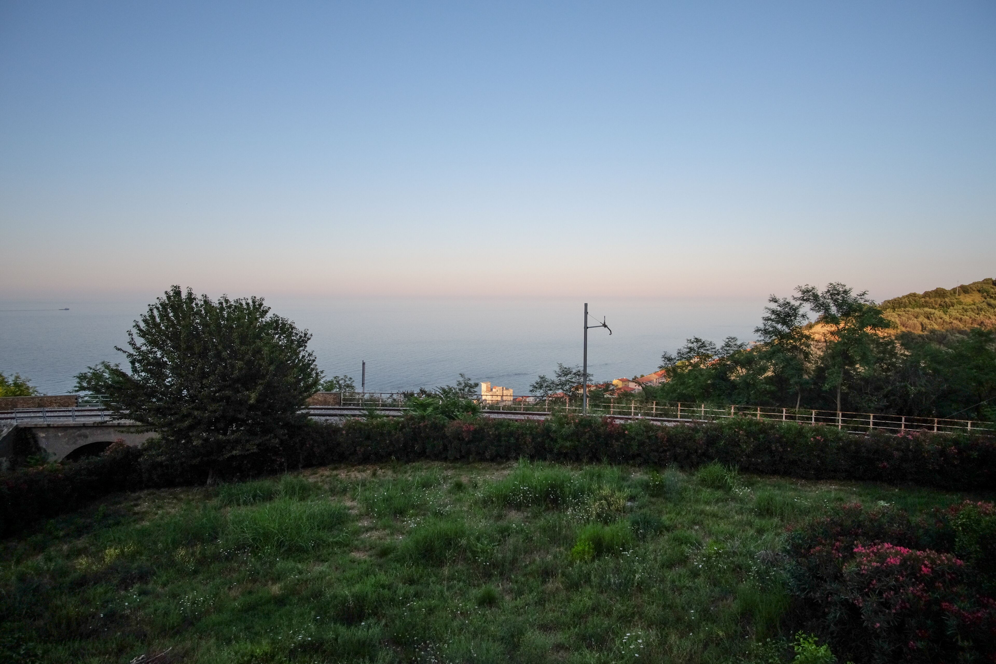 Paesaggio costiero con un ponte, vegetazione e una vista limpida sul mare.