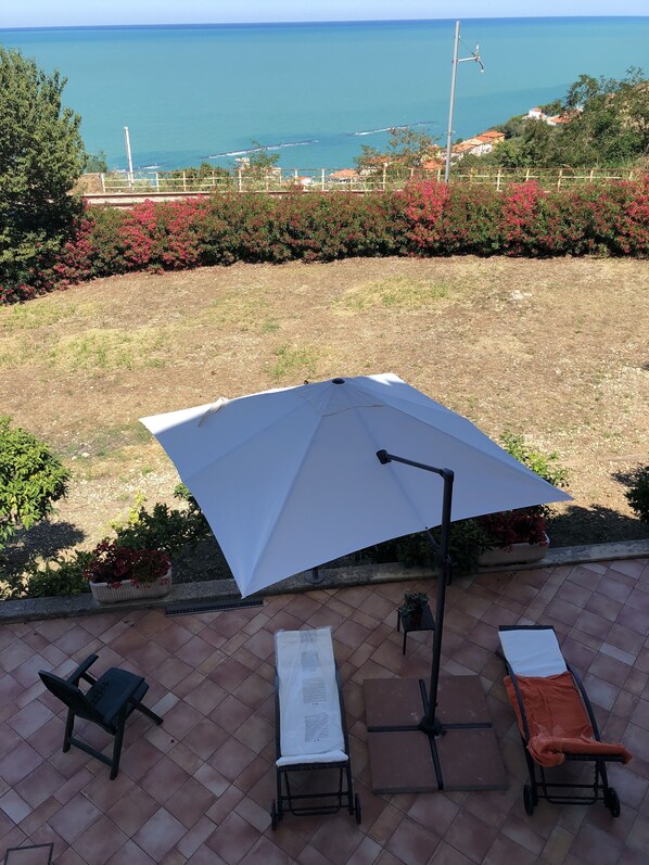 A patio with a large umbrella, two lounge chairs, and a baby stroller.