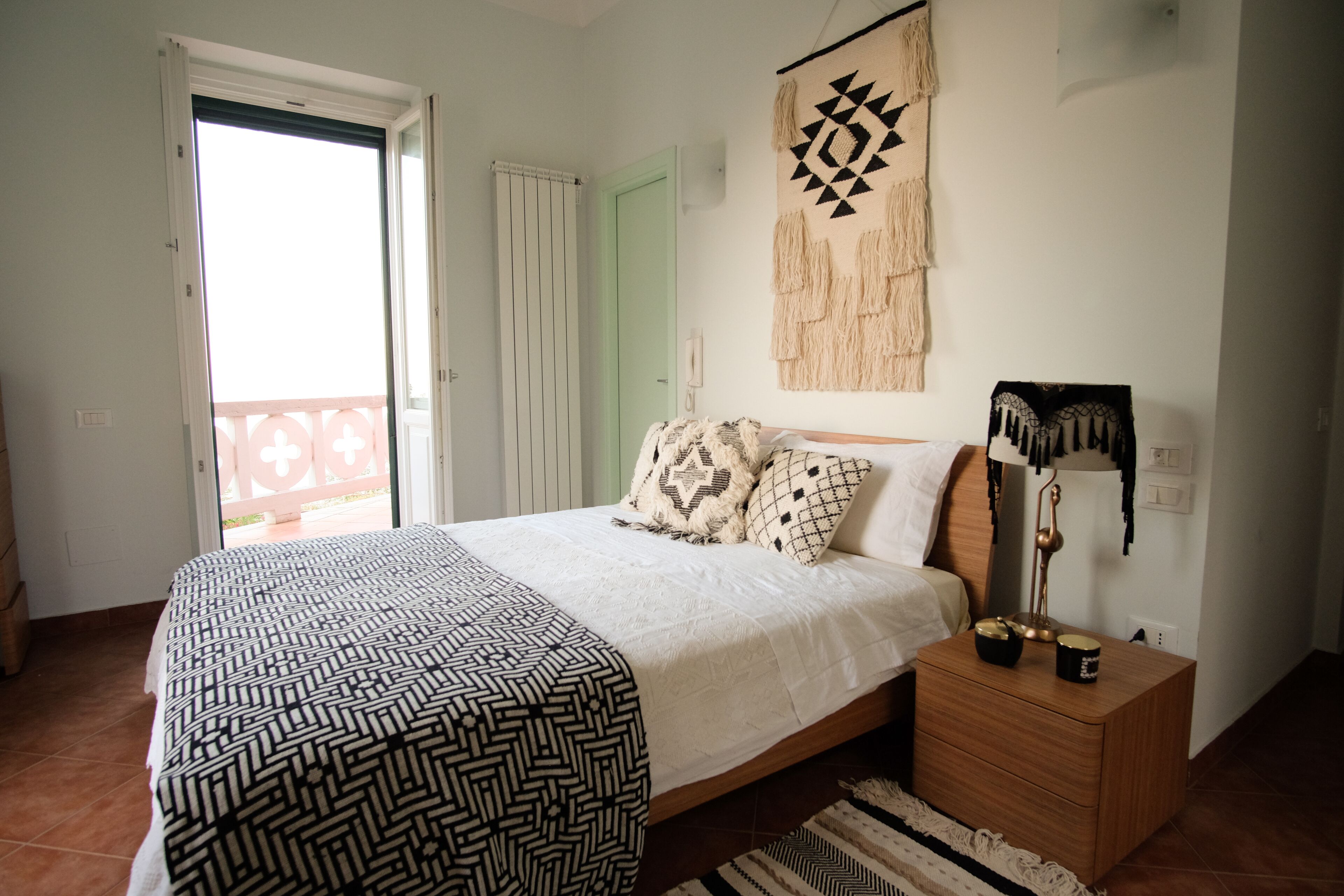 A bedroom with a bed, a nightstand, a wall hanging, and a door to a balcony.