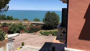 Une vue sur la mer, prise depuis un bâtiment doté d’un balcon surplombant un espace aménagé avec des plantes en pot et une statue.