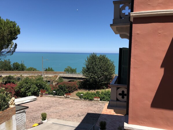 Vista del mar desde un edificio con balcón sobre una zona pavimentada, con macetas y una estatua.