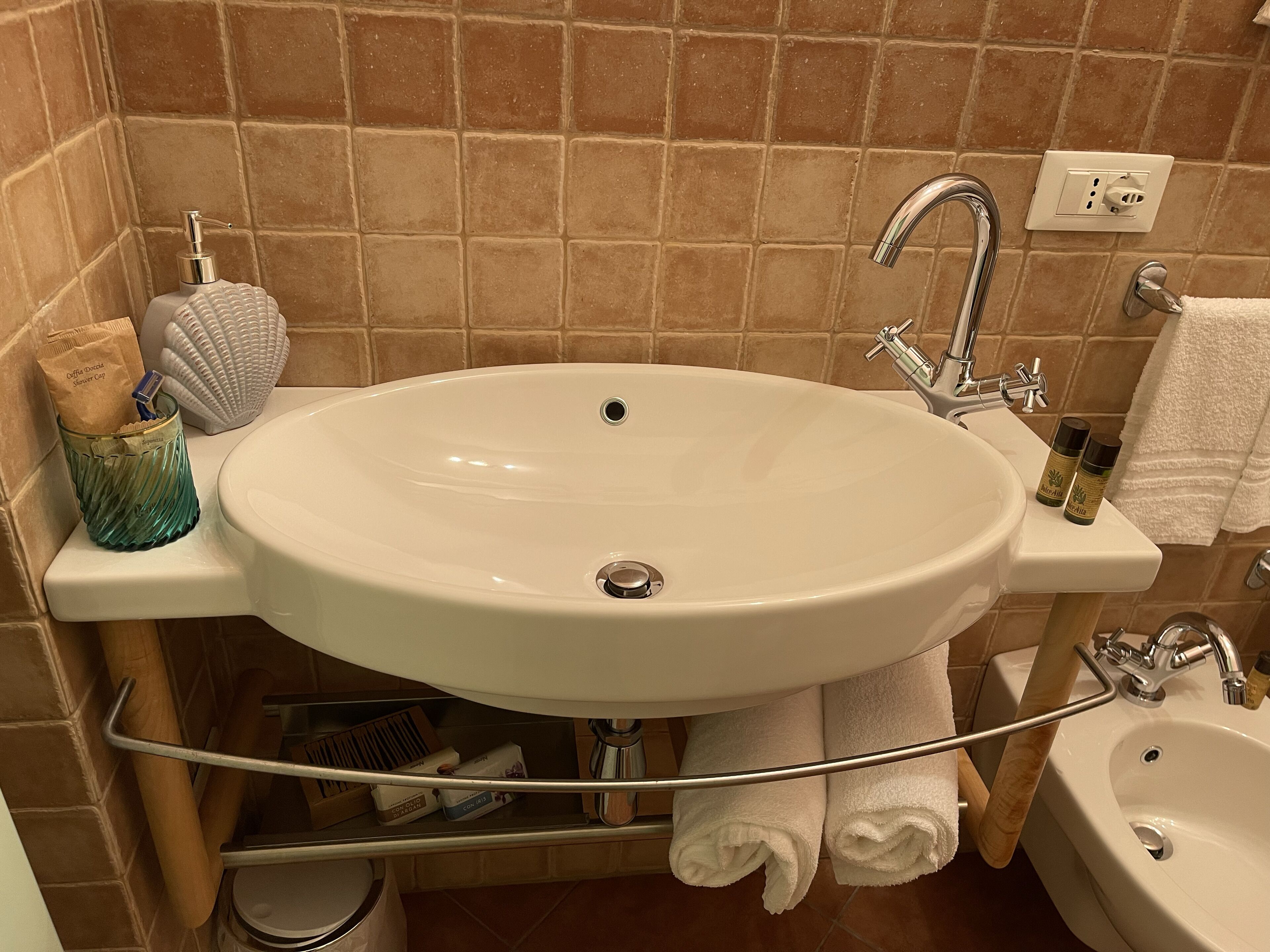 Un bagno con un lavandino bianco capiente, uno specchio, un portasciugamani e una vasca da bagno piccola.