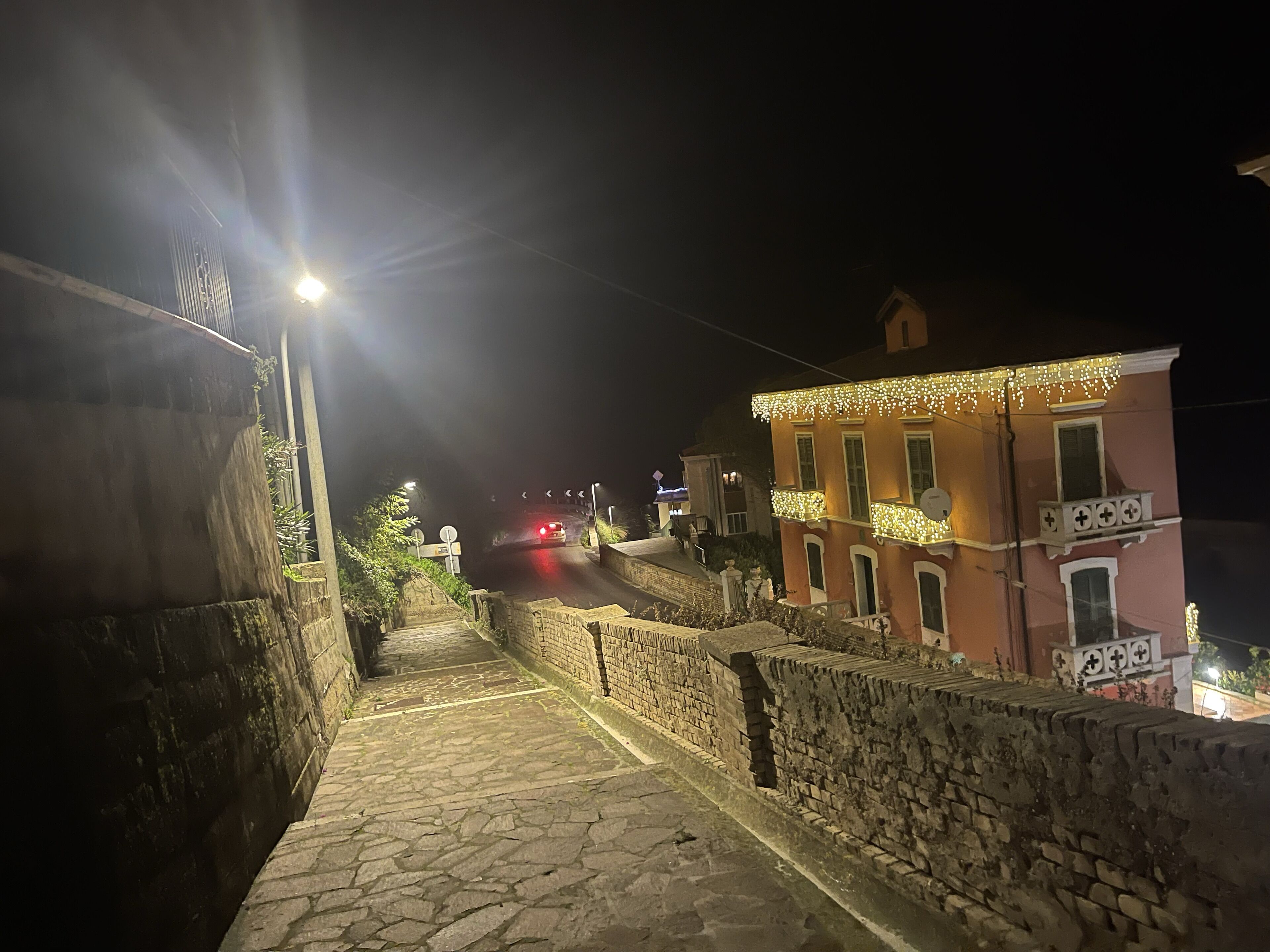 Una escalera de piedra que sube hacia un edificio con balcón, iluminado por farolas.
