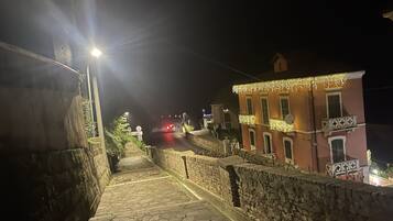 Una escalera de piedra que sube hacia un edificio con balcón, iluminado por farolas.