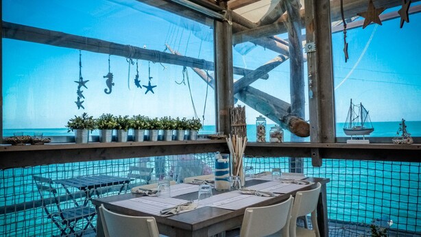 Un coin repas avec vue sur l’océan, comprenant une table dressée pour deux personnes, des chaises et des éléments de décoration sur le thème de la marine.