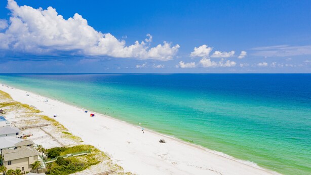 Una playa con agua turquesa cristalina, arena blanca y algunas sombrillas.