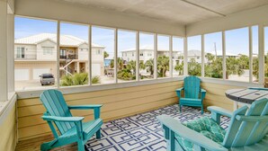 Un espacio exterior techado con vistas a un barrio residencial, que incluye una terraza de madera, sillas Adirondack turquesa y una mesita.
