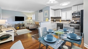 Une cuisine moderne avec des meubles blancs, un coin repas avec de la vaisselle bleue et un salon avec un canapé et un téléviseur.