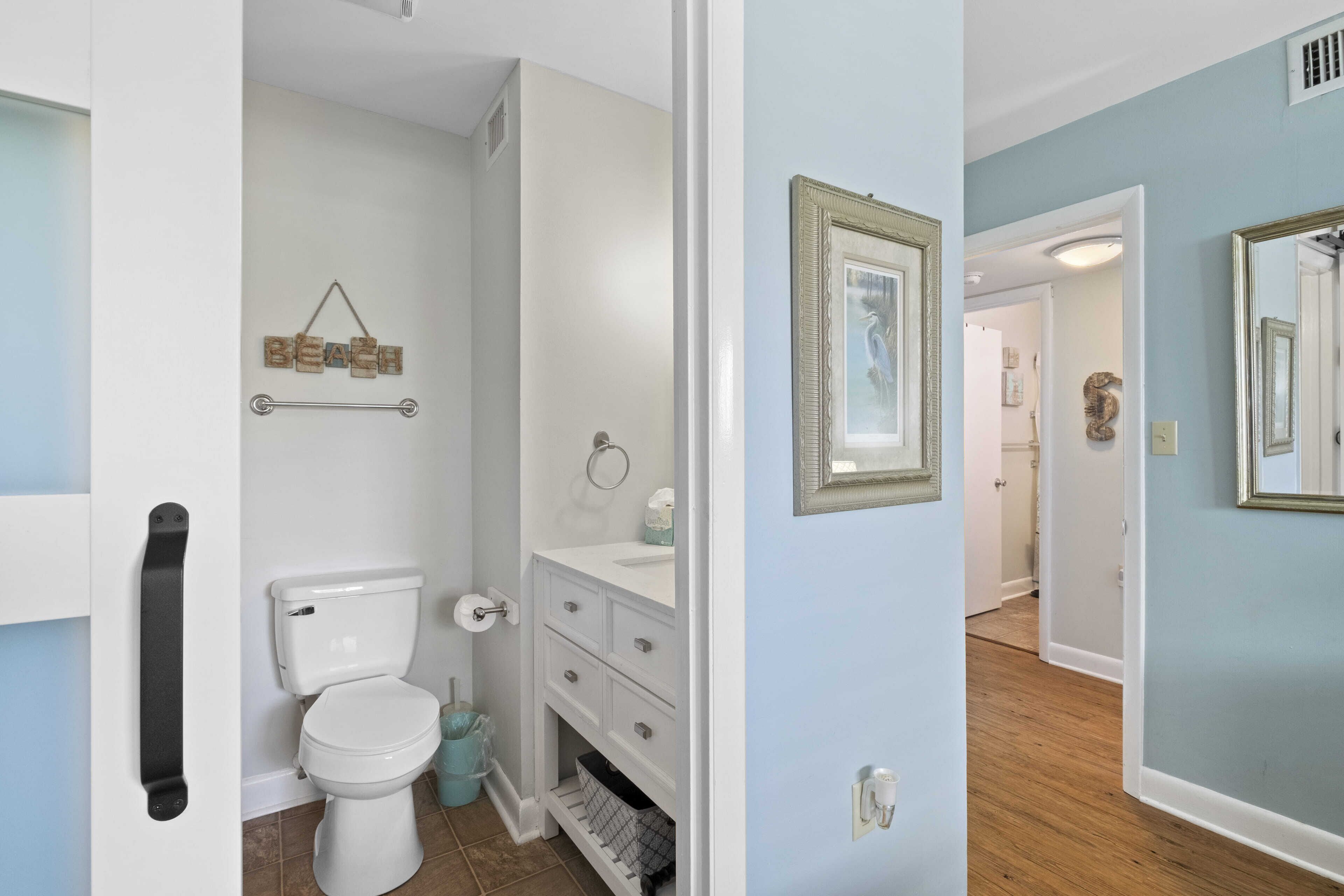 Een badkamer met toilet, wastafel en opbergmeubel. Boven het toilet bevindt zich een handdoekhouder en aan de muur hangt een afbeelding in een lijst.