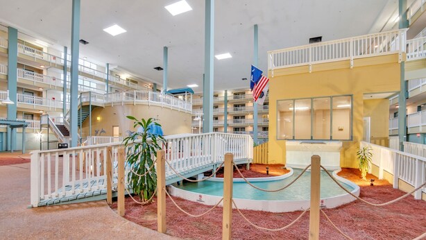 Un atrium intérieur à plusieurs niveaux, doté d’un espace central avec piscine, entouré de rampes en bois et d’une barrière faite de cordes.