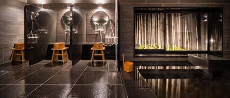 A modern bathroom with dark tiled floors, wooden stools, and a large mirror.