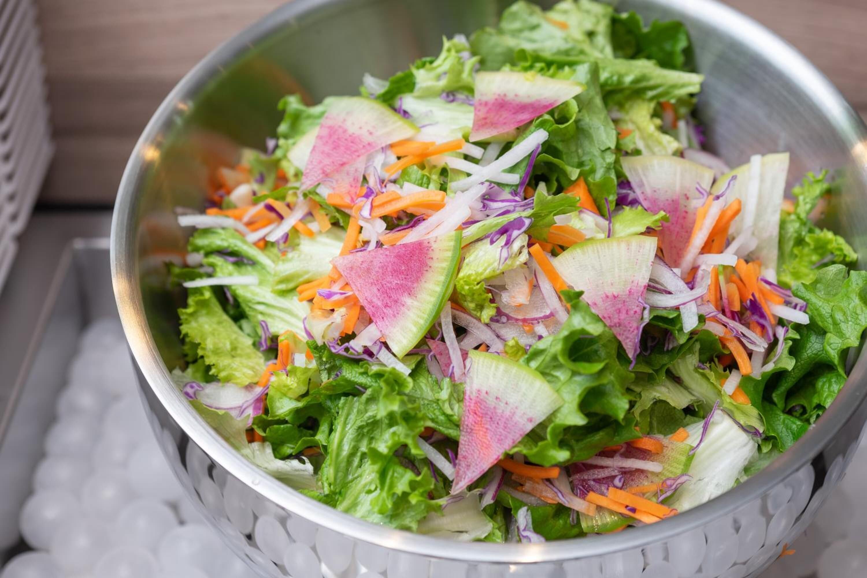 A metal bowl filled with a salad containing lettuce, radishes, and shredded carrots.