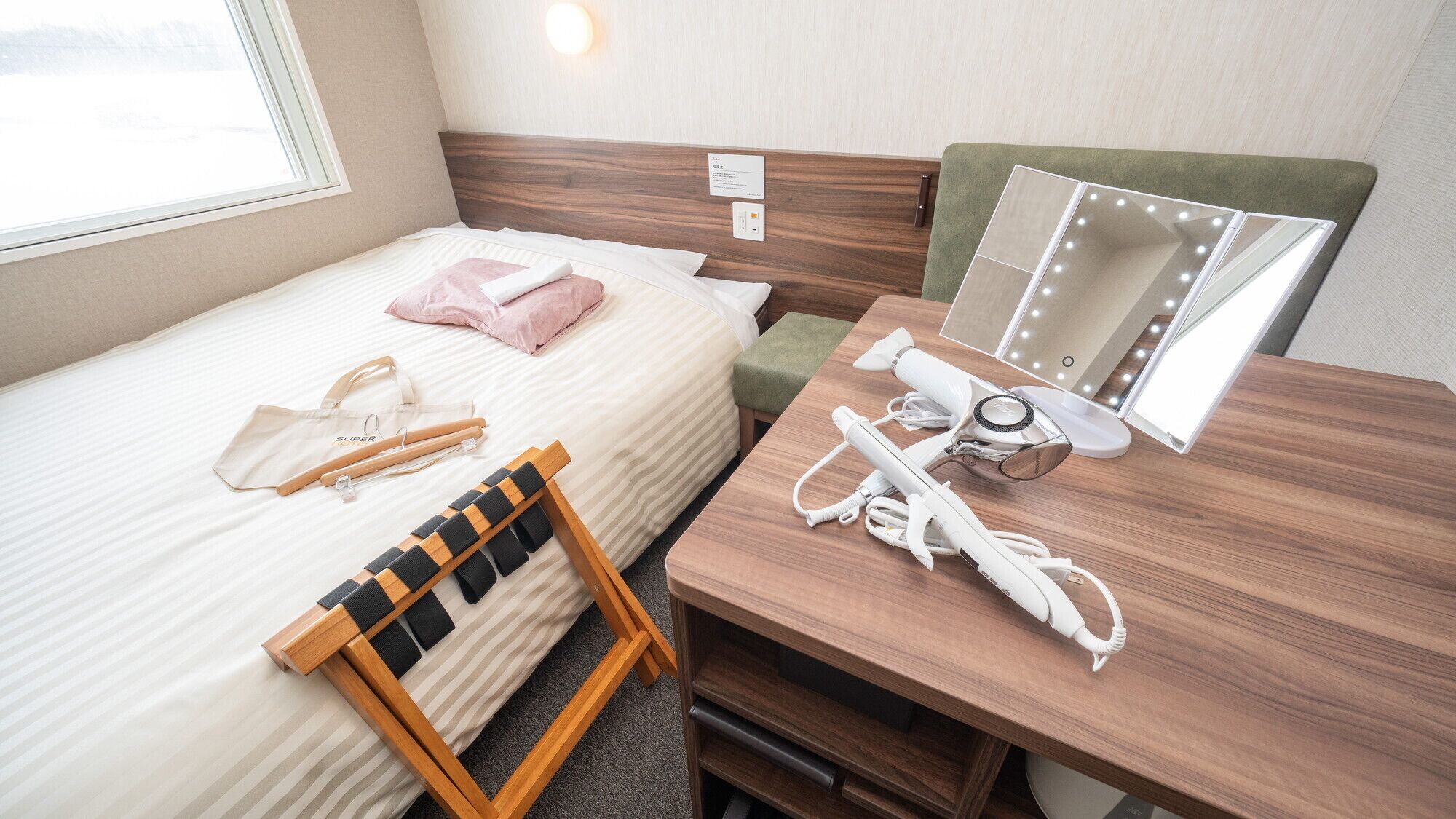 A hotel room with a bed, a wooden desk with a mirror, a hairdryer, and a suitcase.