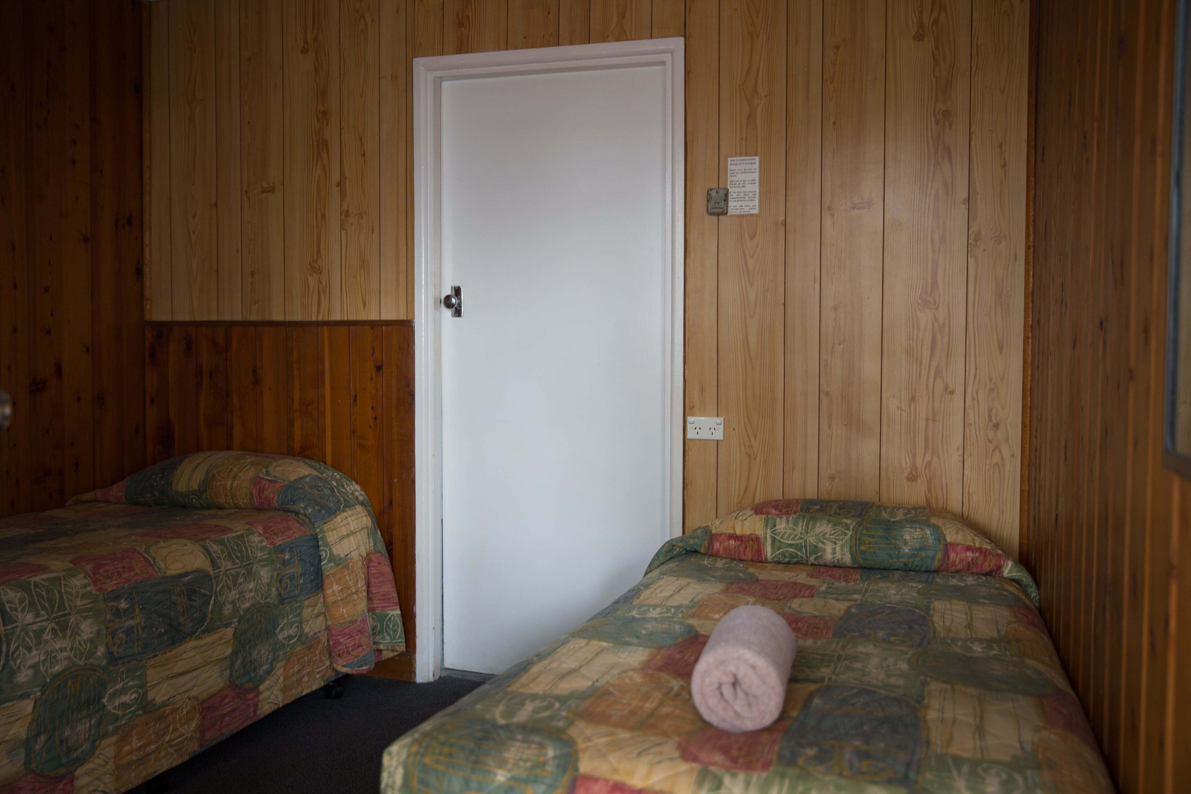 A room with two beds, wooden walls, and a white door.
