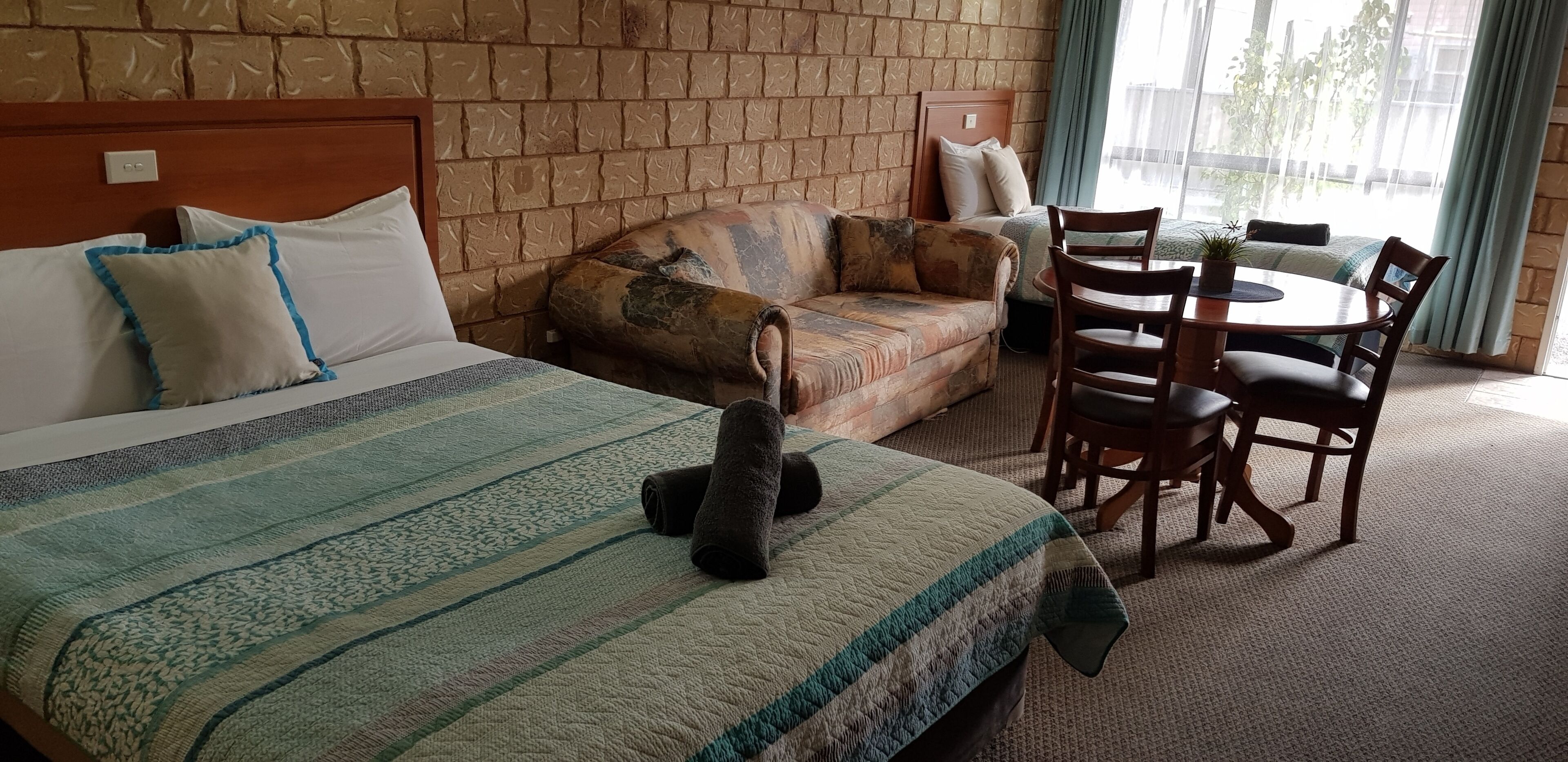 Habitación de hotel con una cama grande, un sofá, una mesa de comedor con sillas y vistas al exterior por una ventana.