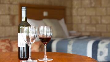 A bottle of wine and two wine glasses on a wooden table in a hotel room with a brick wall and a bed in the background.