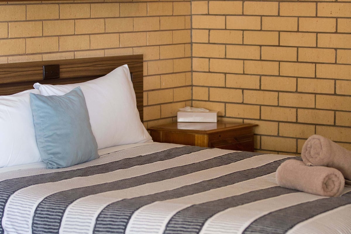 Una cama bien hecha con ropa de cama a rayas, un cabecero de madera y dos almohadas.
