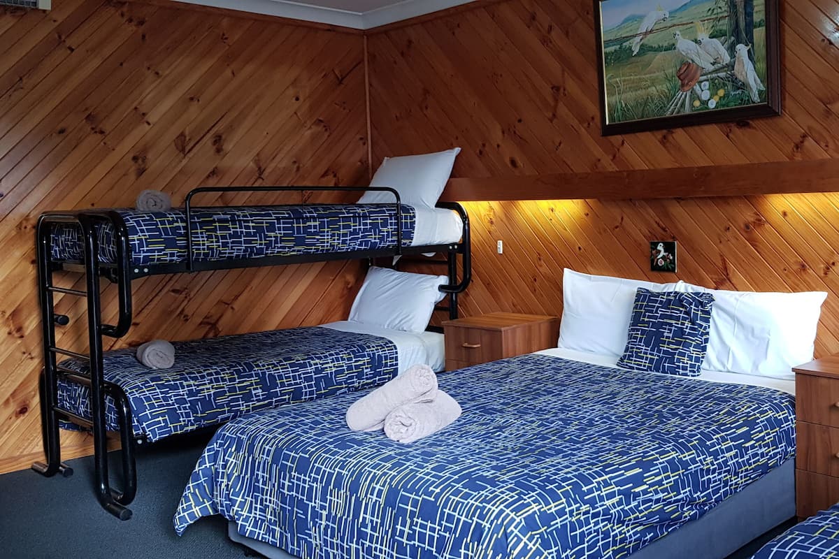 Una habitación con paredes de madera, literas, una mesita de noche y un cuadro.
