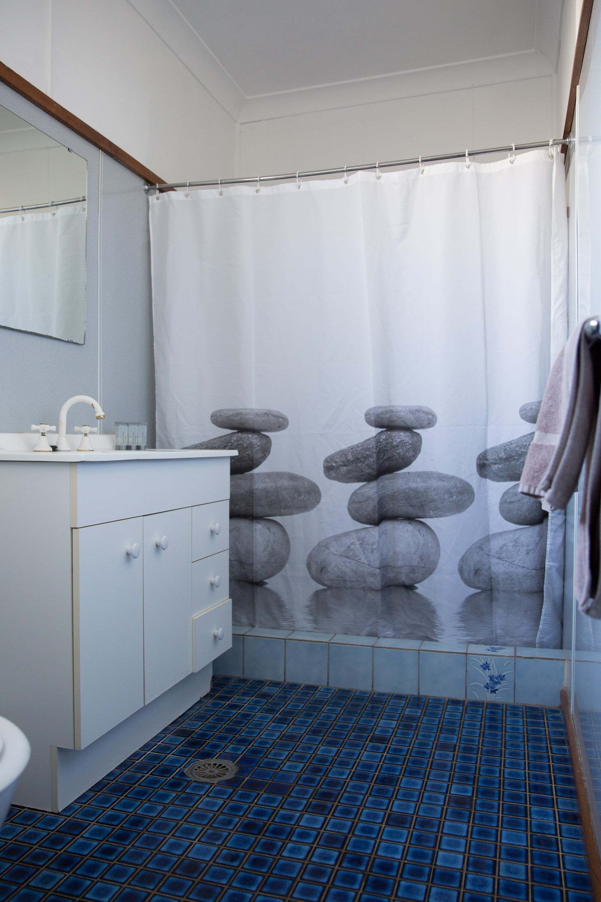 A bathroom with a white sink, a mirror, a blue-tiled floor, and a shower curtain with a rock pattern.