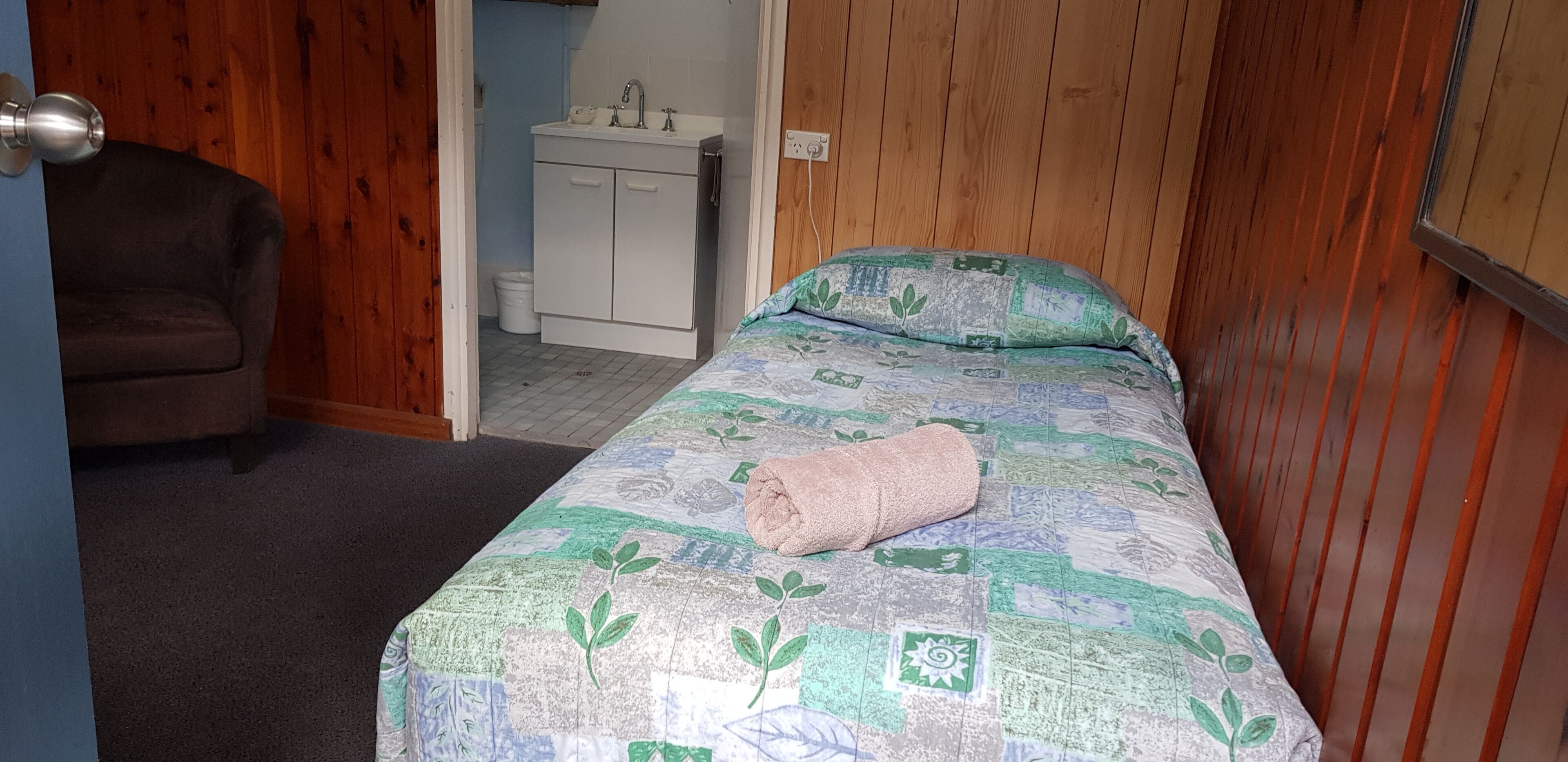 Une petite pièce confortable, avec un lit, une chaise et un mur en bois.