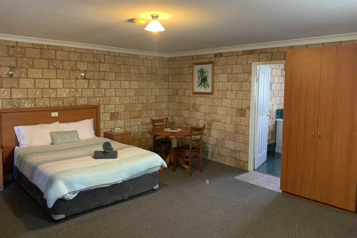 Un dormitorio con cama, una mesa y una silla. Hay una puerta que da a un baño.